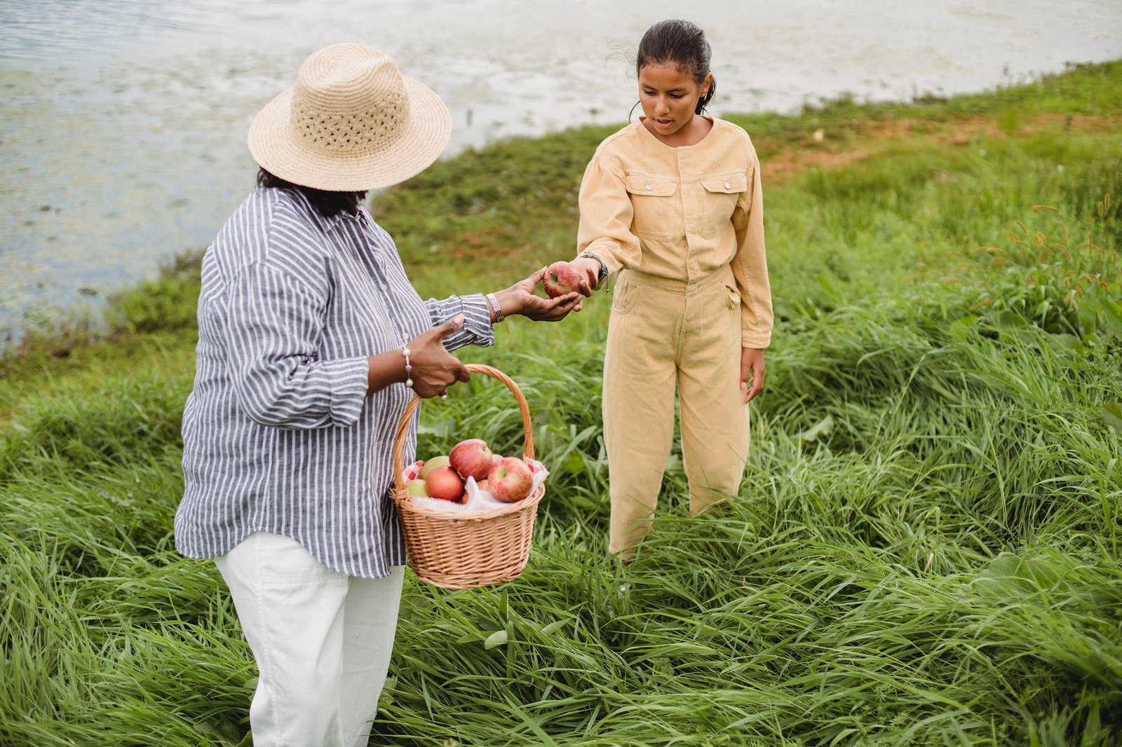 anonymous woman treating girl with apple on river bank